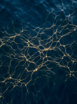 Top-down view of golden caustic light patterns on deep blue ocean