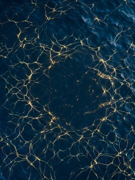 Top-down view of golden caustic light patterns on deep blue ocean