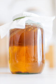 Closeup amber kombucha jar with cloth cover and visible scoby for homemade probiotic drink recipe and kitchen wellness banner