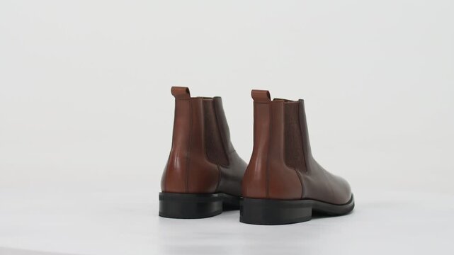 Brown leather men's Chelsea boots rotating on a turntable isolated on a white background, showcasing footwear fashion