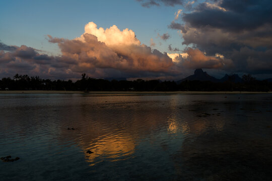 Aerial view of dramatic sunset clouds reflecting on calm coastal waters with silhouetted mountains in the background in Moka District, Mauritius.