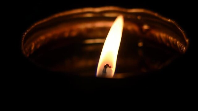 Close-up of a flickering flame in a small l oil lamp illuminates the dark background, creating a warm and spiritual