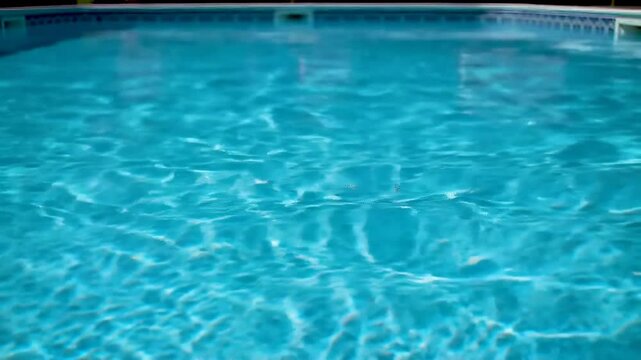Sunlight dances across the surface of a clear blue swimming pool, creating a mesmerizing pattern of light and shadow.