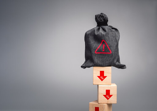 Financial crisis concept with warning icon on money bag on declining percentage blocks. Investment loss, economic downturn, revenue decline and financial instability risk in business environment.