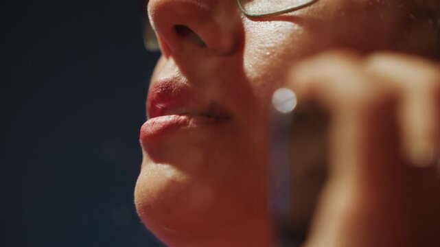 Low angle lips near microphone speaking closely, intense rehearsal or recording session with glasses catching warm stage light, visible sweat and skin texture, hand holding small microphone,