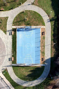 Aerial view of a blue basketball court surrounded by a gravel walking path and green lawn in Turin, Piedmont, Italy.
