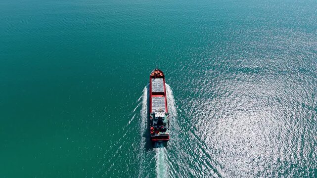 Beautiful waterscape sparkling in the sun crossed by the large bulk carrier. Drone footage following a ship in a voyage.