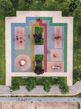 Aerial view of a colorful children's playground with geometric patterns, swings, and a carousel surrounded by green grass and trees in Turin, Piedmont, Italy.