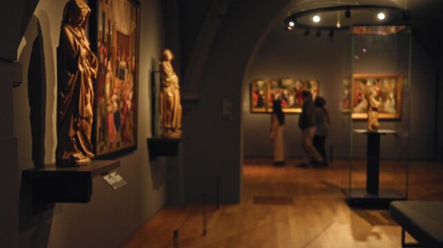 Museum gallery with blurred figures viewing statues and paintings in dimly lit indoor setting evokes sense of quiet contemplation.