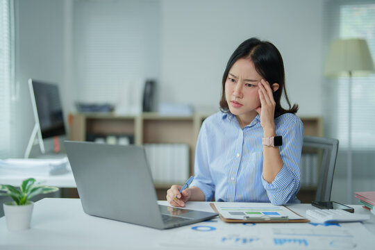 Asian businesswoman dealing with stress and headache at work, experiencing burnout and pressure while working on laptop in modern office, feeling overwhelmed and exhausted