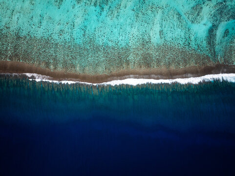 Aerial view of the vibrant coral reef and deep blue ocean waters with white surf breaking along the reef edge in Moorea-Maiao, Windward Islands, French Polynesia.