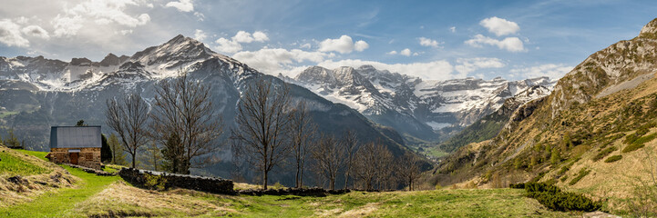 Fototapeta premium Panoramic view of a small stone cottage high in the French Pyrenees with the peak of the mountain, Piméné, behind and the Cirque de Gavarnie in the distance