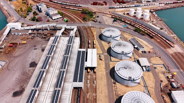 Railways crossing the territory of a modern port along the warehouses and metal tanks. Commercial facility for global trading from drone.