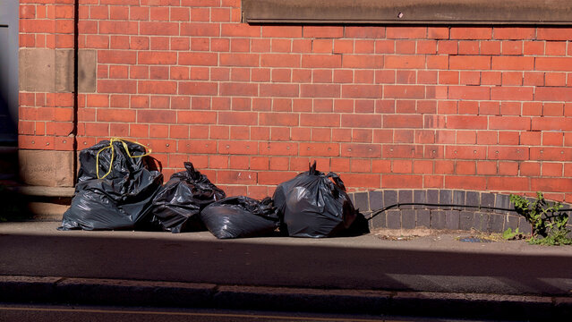 Garbage bags on street, black trash sacks near brick wall, urban waste management, municipal pollution, environmental issues copy space