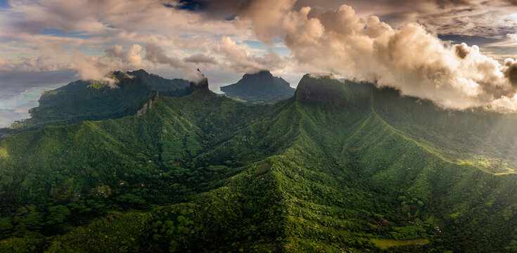 Aerial view of the lush volcanic peaks and dense tropical forests under dramatic clouds at sunset Moorea-Maiao, Windward Islands, French Polynesia.