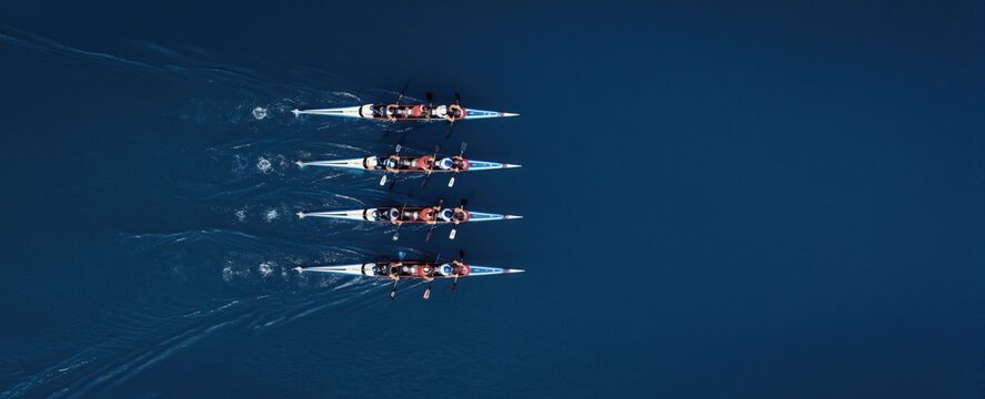 Synchronized rowing team paddles kayaks in unison across deep blue water. Athletes train together in race boats striving for speed and teamwork success.