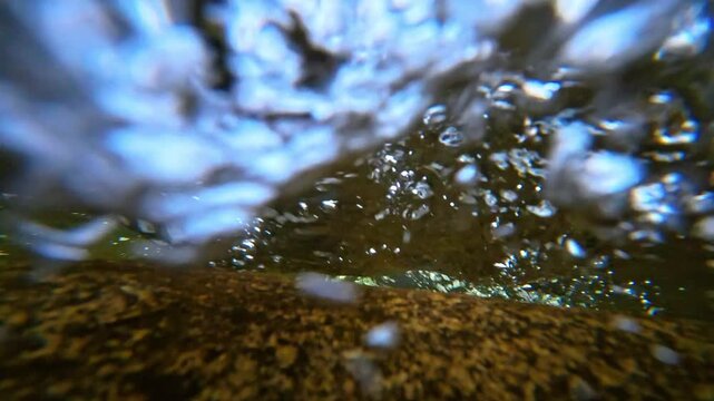 Underwater view of turbulent rushing stream water with air bubbles. Close-up underwater abstract shot of bubbles and moving water over a stony riverbed at Mount Tammany.