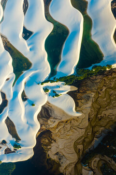 Aerial view of the white sand dunes and turquoise lagoons of Parque Nacional dos Lencois Maranhenses with a winding river and green vegetation in Lencois Maranhenses, MA, Brazil.
