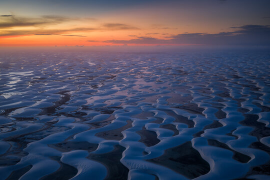 Aerial view of the white sand dunes and lagoons of Parque Nacional dos Lencois Maranhenses under a sunset sky in Lencois Maranhenses, MA, Brazil.