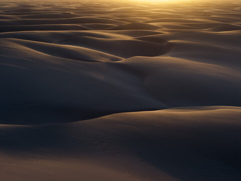Aerial view of the vast sand dunes of Parque Nacional dos Lencois Maranhenses with golden sunset light hitting the crests and deep shadows Lencois Maranhenses, MA, Brazil.