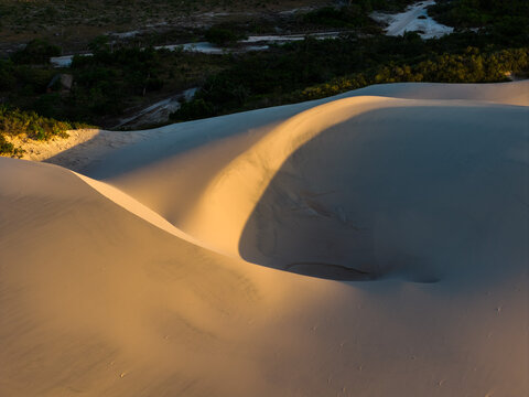 Aerial view of the white sand dunes of Parque Nacional dos Lencois Maranhenses with golden sunlight and deep shadows at sunset Lencois Maranhenses, MA, Brazil.