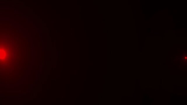 Two red lights blinking on black background creating a minimalist and abstract visual effect.