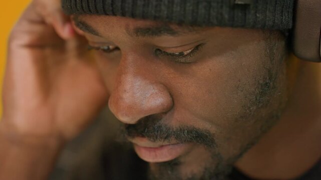 Man adjusting headphones while composing, quiet focus and careful listening, closeup beanie and ear, warm yellow studio, melodic refinement, calm creative atmosphere, attentive portrait