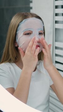 Lovely young beautiful girl applying cosmetic moisturizing face mask in bathroom at home. Preteen girl skin care treatment. Slow motion