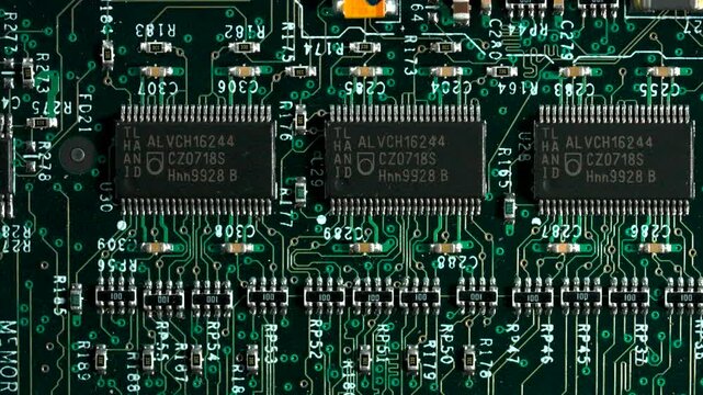 High angle detailed shot of a green computer motherboard showing transistors and integrated circuits.