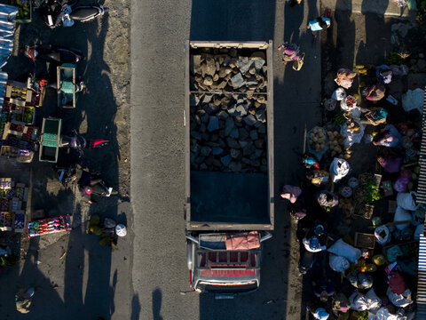 Aerial view of a truck carrying stones through a busy roadside market with people and stalls in Kemalang, Central Java, Indonesia.