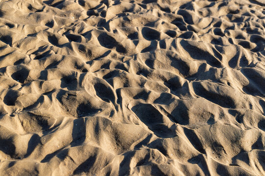 Texture of messy trampled sand on a beach with footprints and shadows.
