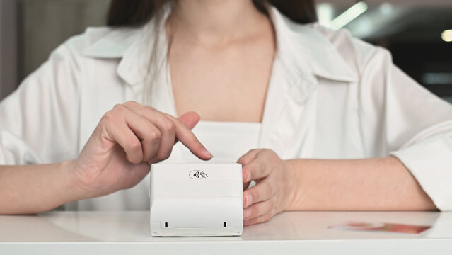  A seller with a wireless payment terminal and a buyer paying for a service or product, applying a card to the POS terminal, close-up of a hand