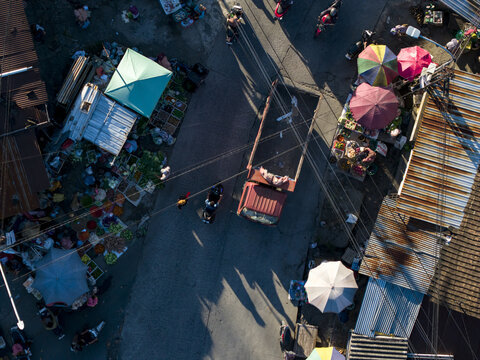 Aerial view of a bustling street market with a red truck, motorbikes, and colorful stalls under morning light in Kemalang, Central Java, Indonesia.