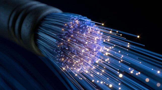 Close-up of a fiber optic cable end, where many thin strands emit bright yellow sparks of light against a dark, cool blue background.