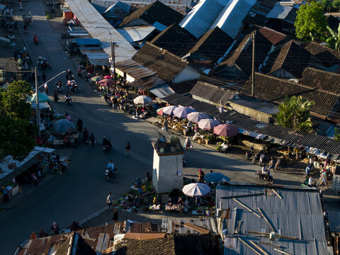 Aerial view of a bustling street market with vendors under colorful umbrellas, motorbikes, and traditional dark-tiled rooftops Kemalang, Central Java, Indonesia.