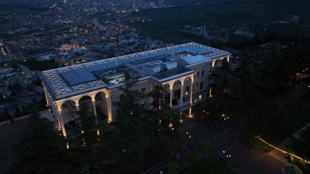 Aerial night view of Mtatsminda Park restaurant and funicular station in Tbilisi, Georgia, featuring illuminated arched architecture