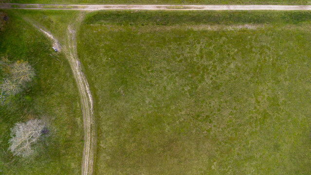 Top down aerial view of a green meadow with a dirt path intersection and a lonely bench. Minimalist rural landscape captured from above, showcasing texture, geometry, and peaceful countryside.