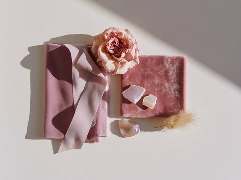 Overhead flat lay of pink fabric, dried flower, and decorative elements on pure white background, ideal for mood board or design inspiration