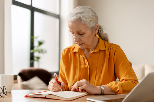 Senior woman planning tasks in home office taking notes