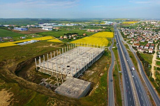 Aerial view of a large concrete building frame under construction next to a highway and yellow canola fields in Silivri, Istanbul, Turkey.