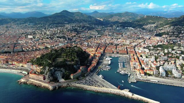 4K aerial view of Port Lympia marina in Nice with Castle Hill, Rauba-Capeu war memorial, Old Nice, breakwater and Maritime Alps mountain range backdrop on the French Riviera.