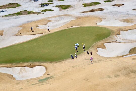 Aerial view of golfers and caddies on a putting green surrounded by extensive sand bunkers and dry grass in Juno Beach, Florida, United States.