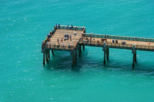 Aerial view of Juno Beach Pier with people fishing on the wooden deck over turquoise ocean waters in Juno Beach, Florida, United States.