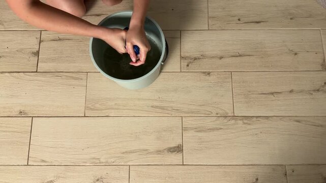 Woman Diligently Rinses And Wrings Cloth Over Bucket Beside Kitchen Cabinets With Steady Hands