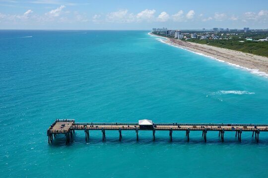 Aerial view of the Juno Beach Pier stretching into turquoise ocean waters along the sandy coastline with people fishing in Juno Beach, Florida, United States.