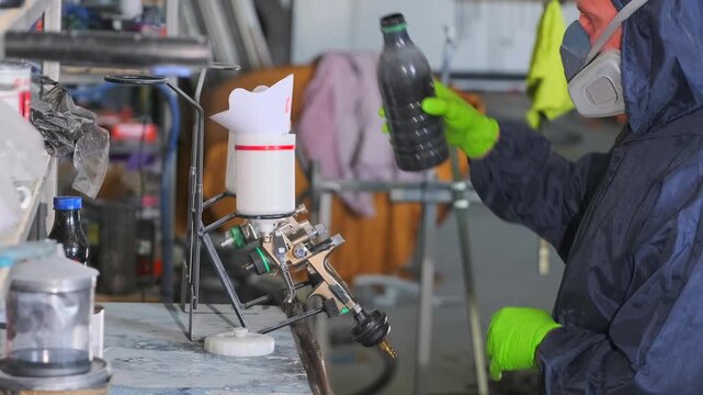 Auto body repair technician pouring automotive paint into spray gun container during vehicle refinishing and professional car painting preparation in workshop. Paint mixing for spray gun