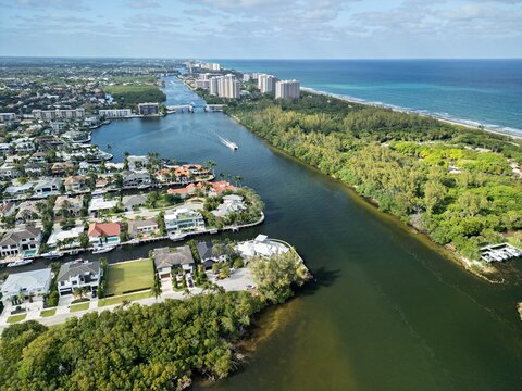 Aerial view of the Intracoastal Waterway with luxury waterfront homes, dense tropical greenery, and high-rise buildings along the Atlantic coastline in Boca Raton, Florida, United States.