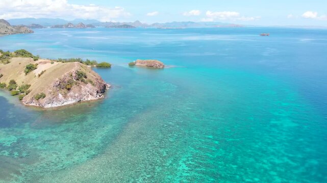 Aerial view of the northern headland near Labuan Bajo in Komodo National Park, Indonesia, surrounded by vibrant coral reefs and turquoise tropical waters under a sunny blue sky
