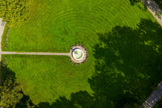 Aerial view of a circular stone fountain centered in a lush green lawn with concentric mowing patterns in Taujenai, Vilnius County, Lithuania.