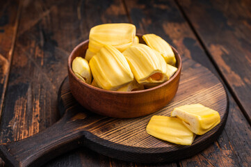 Sweet, golden jackfruit pods (bulbs) in a wooden bowl on a rustic dark wood table. Tropical fruit snack with copy space. © Mironov